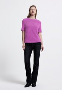 Fuchsiový krátký rukávový top s texturovaným povrchem, spárovaný s černými rovnými džíny. Oblečení doplňují černé špičaté boty.