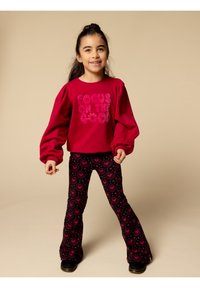 Rode top met lange mouwen en pofmouwen, met de tekst "FOCUS ON THE GOOD". Zwarte uitlopende leggings met een roze hartjespatroon. Zwarte schoenen.