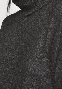 Kolgrå polotröja i mjukt, fuzzigt material. Har en hög krage och mönstrad stickning. Inga synliga detaljer.