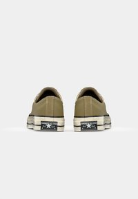 Baskets en toile khaki clair avec semelles en caoutchouc blanc, accents noirs et un logo étoile classique au talon. Texture lisse avec des détails cousus.
