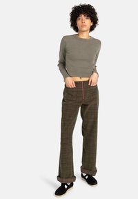 Un haut à manches longues crop en vert olive associé à un pantalon large à carreaux avec une fermeture éclair devant, des poignets retroussés et des chaussures noires.