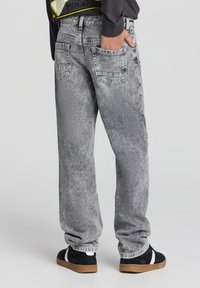 Jeans in denim grigio con una finitura sbiadita, vestibilità rilassata, cinque tasche e gamba affusolata. Indossati con sneakers nere e bianche.