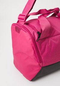 Ružová športová taška s textúrovaným povrchom, s čiernym dnom, nastaviteľnými popruhmi a zipsovým vreckom.