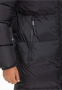 Doudoune noire avec un design matelassé, dotée d'une poche zippée sur le côté gauche et d'une texture lisse et brillante.