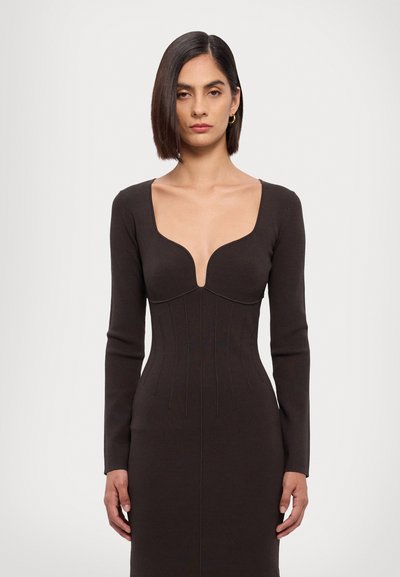 Abito lungo marrone a maniche lunghe con scollatura a V profonda, texture a coste e silhouette aderente. Presenta cuciture verticali che creano un design strutturato.