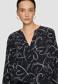 Blouse bleu marine avec un motif de cœur blanc et d'écriture, décolleté en V et manches longues, fabriquée à partir d'un tissu léger avec une texture lisse.