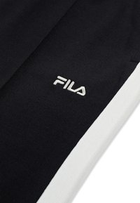 Zwart stof met witte streep toont wit geborduurd FILA-logo, een close-up van sportkledingmateriaal en branding.