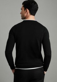 Pulover negru, ajustat, confecționat dintr-un material moale, cu mâneci lungi, decolteu rotund și tiv ribetat, purtat peste o cămașă albă și pantaloni.