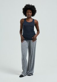 Schwarzes Tanktop mit einem taillierten Design, kombiniert mit lockeren, hellgrauen, strukturierten, weiten Hosen. Das Model steht mit den Händen in die Hüften gestützt.