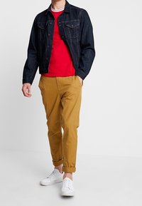 Chaqueta de denim en azul oscuro, camiseta de cuello redondo roja, pantalones caqui ajustados y zapatillas blancas. Cuenta con puños enrollados y un diseño clásico de bolsillo.