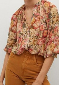 Blouse florale en tissu léger et transparent, ornée de fleurs rouges, roses et jaunes, avec un col en V, un col froncé et des manches courtes.