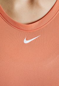 Top atletico arancione Nike con scollo rotondo, texture liscia e piccolo logo swoosh bianco sul petto.
