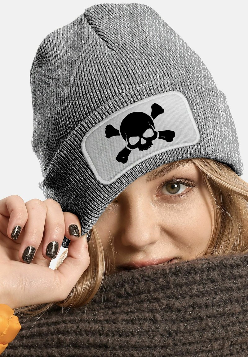 Gray knitted beanie with a large, white rectangular patch featuring a black skull and crossbones design. Textured fabric and fitted shape.