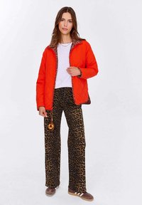 Czerwona pikowana kurtka z wyściółką w leoparda, zestawiona z szerokimi spodniami w brązowy i czarny wzór leoparda. Brązowe sneakersy i dodatki.