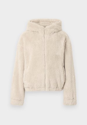 Beige capuchonjas van zacht, pluizig materiaal. Voorzien van een volledige ritssluiting aan de voorkant, lange mouwen en een iets kortere zoom.