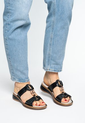 Fødder iført lyseblå jeans og sorte kilehælssandaler med perledekorationer og rød neglelak på tæerne.