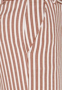 Tissu rayé en beige et rouille, avec des lignes verticales étroites. Le matériau semble tissé, présentant une finition texturée. Présente un design ajusté.