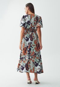 Robe maxi à imprimé floral multicolore, dotée de manches bouffantes, d'une taille smockée et d'un tissu fluide. Fond clair avec des motifs détaillés.