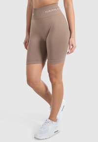 Tan fietsbroek met een brede, geribbelde tailleband met witte "SMILOS" tekst. Gladde stof met een nauwsluitende pasvorm, eindigend net boven de knie.