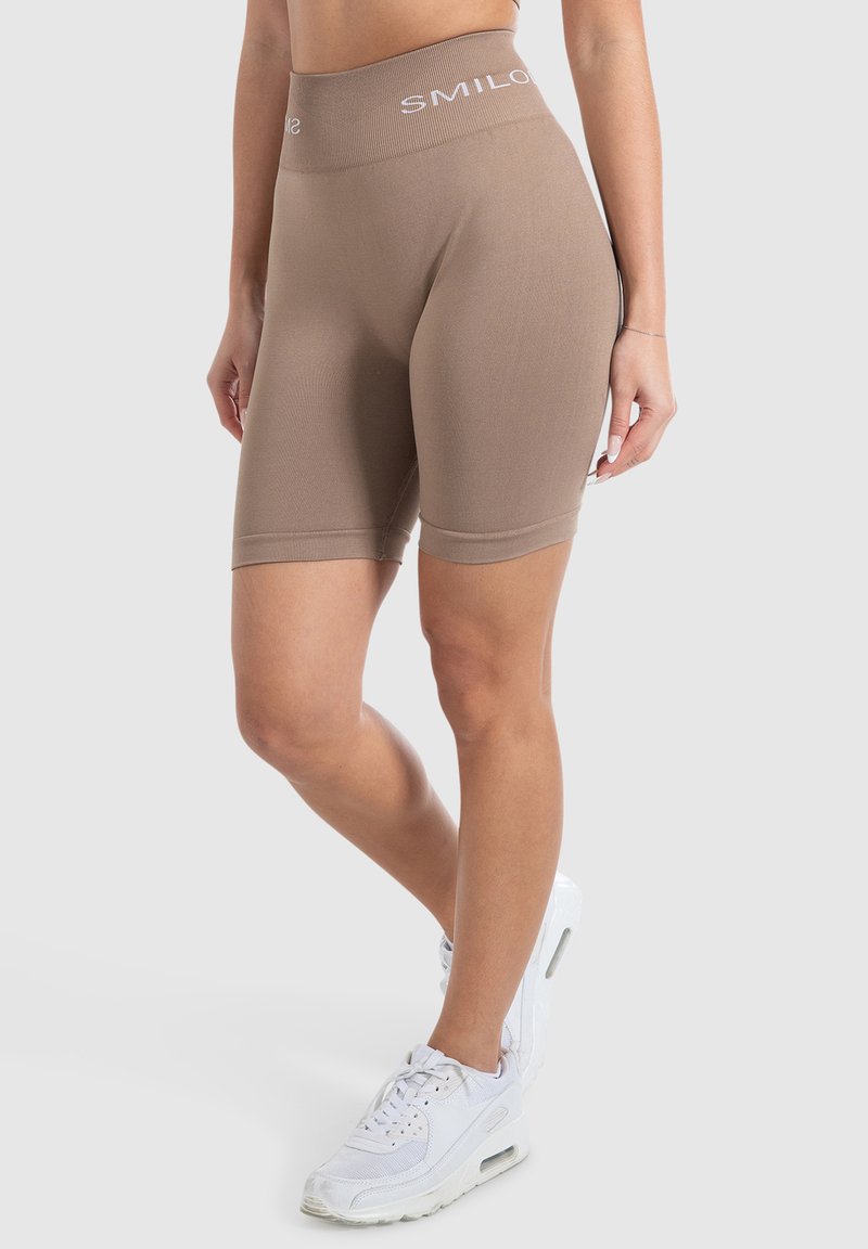 Tan fietsbroek met een brede, geribbelde tailleband met witte "SMILOS" tekst. Gladde stof met een nauwsluitende pasvorm, eindigend net boven de knie.