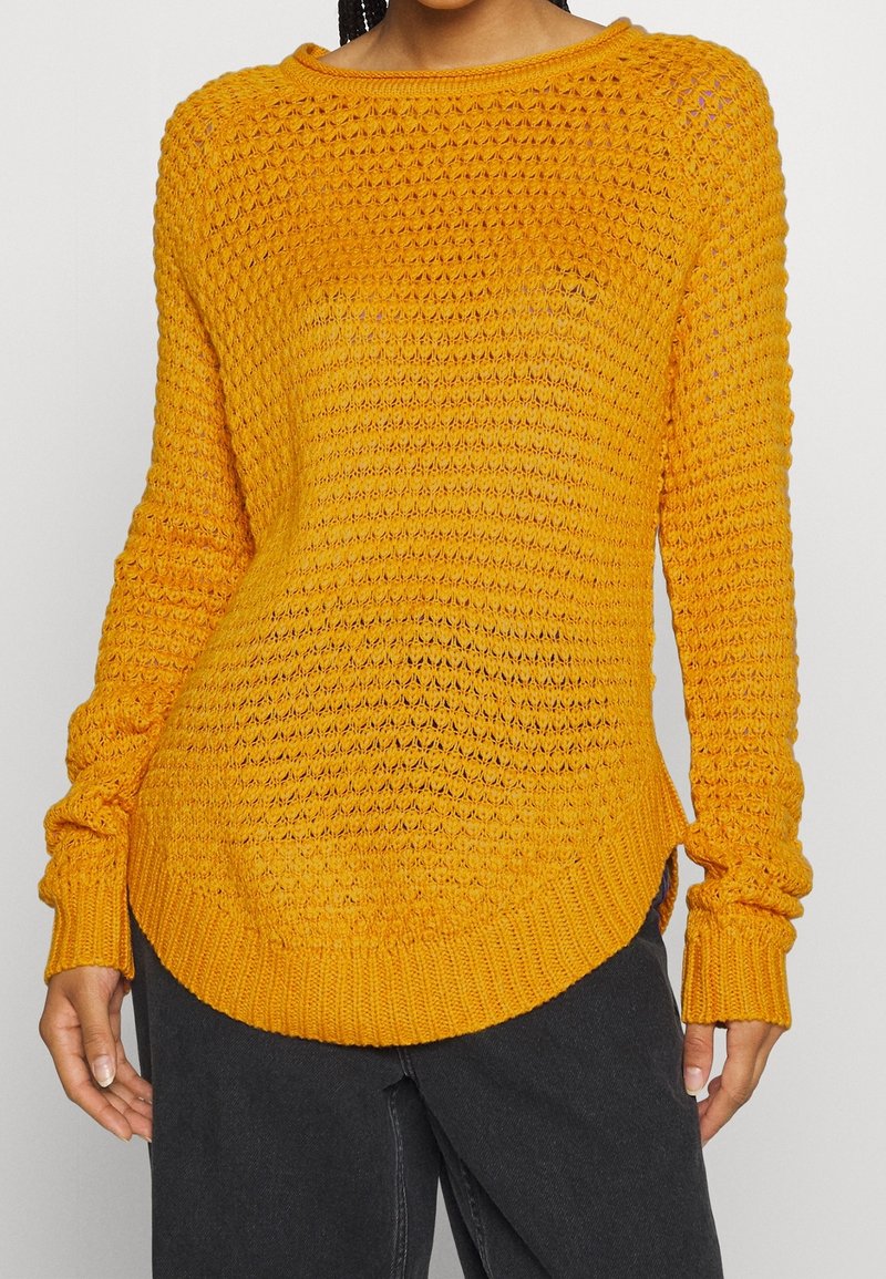 Maglione giallo lavorato a maglia con un motivo testurizzato, scollo rotondo e maniche lunghe con polsini e orlo a coste.