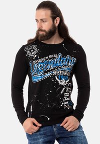 Schwarzes Langarm-T-Shirt mit weißen und blauen Grafikdrucken und Spritzdesigns. Hergestellt aus weichem Stoff, figurbetonte Passform mit rundem Halsausschnitt.