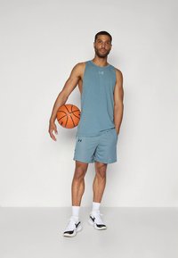 Lichtblauw sportief tanktop en korte broek, gemaakt van ademende stof, gecombineerd met witte sneakers met zwarte accenten; een basketbal vasthoudend.