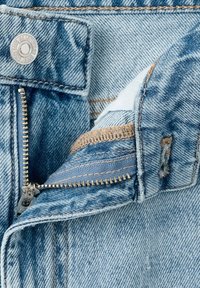 Close-up of open light blue denim jeans zipper and metal button with visible stitching details.