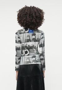 Μπλούζα μακρυμάνικη με εκτύπωση σε ασπρόμαυρο κόμικ; μαλακή υφή; ετικέτα με λογότυπο στο γιακά; φοριέται με μαύρη φούστα.