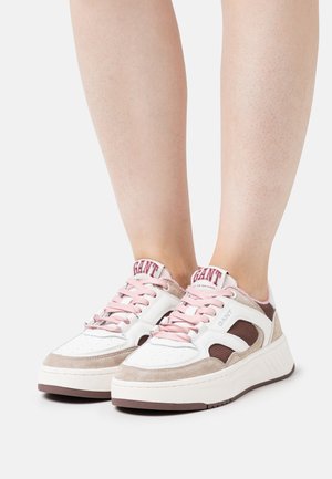 Weiße und beigefarbene Sneaker mit pinken Akzenten, aus strukturiertem Wildleder und Mesh-Materialien, ausgestattet mit einer dicken Sohle sowie einem Logo an der Ferse und Zunge.
