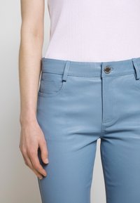 Pantaloni in pelle azzurro chiaro con vestibilità slim, dotati di tasche frontali, chiusura a bottone e dettagli di cucitura a contrasto lungo le cuciture.