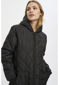 Veste doudoune noire matelassée avec capuche, dotée d'une fermeture éclair à l'avant, de poches latérales et de poignets côtelés. Le matériau semble lisse et brillant.