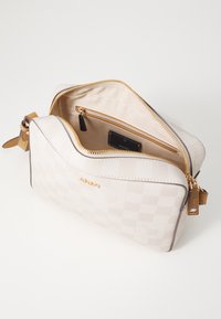 White checkered pattern handbag with gold hardware, open zipper, beige interior lining, and a label visible inside.