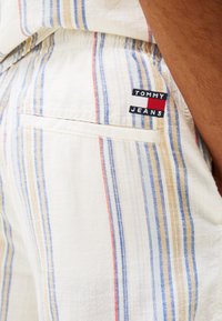 Stripete shorts i lett stoff med blå, gul og rød striper. Inkluderer et lite svart merke med "TOMMY JEANS" brodert på.