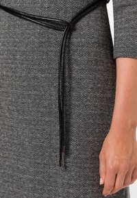 Robe en tissu gris à chevrons avec une ceinture en cuir noire. La ceinture a des embouts en métal argenté et est nouée à la taille. Manches courtes et surface texturée.