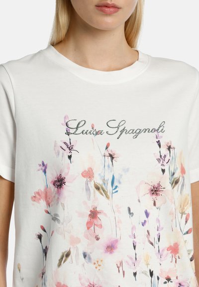 Camiseta de algodón blanca con patrones florales en rosa y púrpura con embellishments. El nombre de la marca "Luisa Spagnoli" se muestra en una fuente delicada.