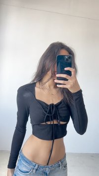 Black ribbed long-sleeve crop top with a front tie detail and cut-out; paired with light blue denim jeans. Smooth texture, fitted design.