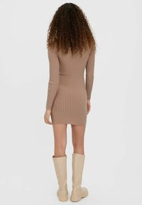 Figurnära ribbad klänning i beige, långärmad, minilängd, med texturerad stickning och sidoislits, tillsammans med knähöga beige stövlar.