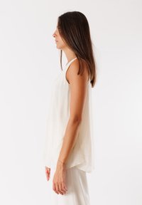 Top senza maniche in crema chiaro, realizzato in tessuto morbido e fluido, con una vestibilità rilassata e orlo arrotondato. Una sottile texture valorizza la sua semplicità.