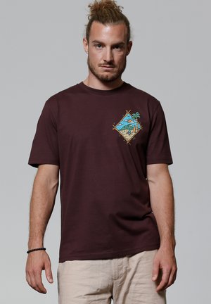 Bordeaux katoenen t-shirt met een kleurrijke gedessineerde afbeelding van palmbomen en een strand in een diamantvorm op de linkerborst.