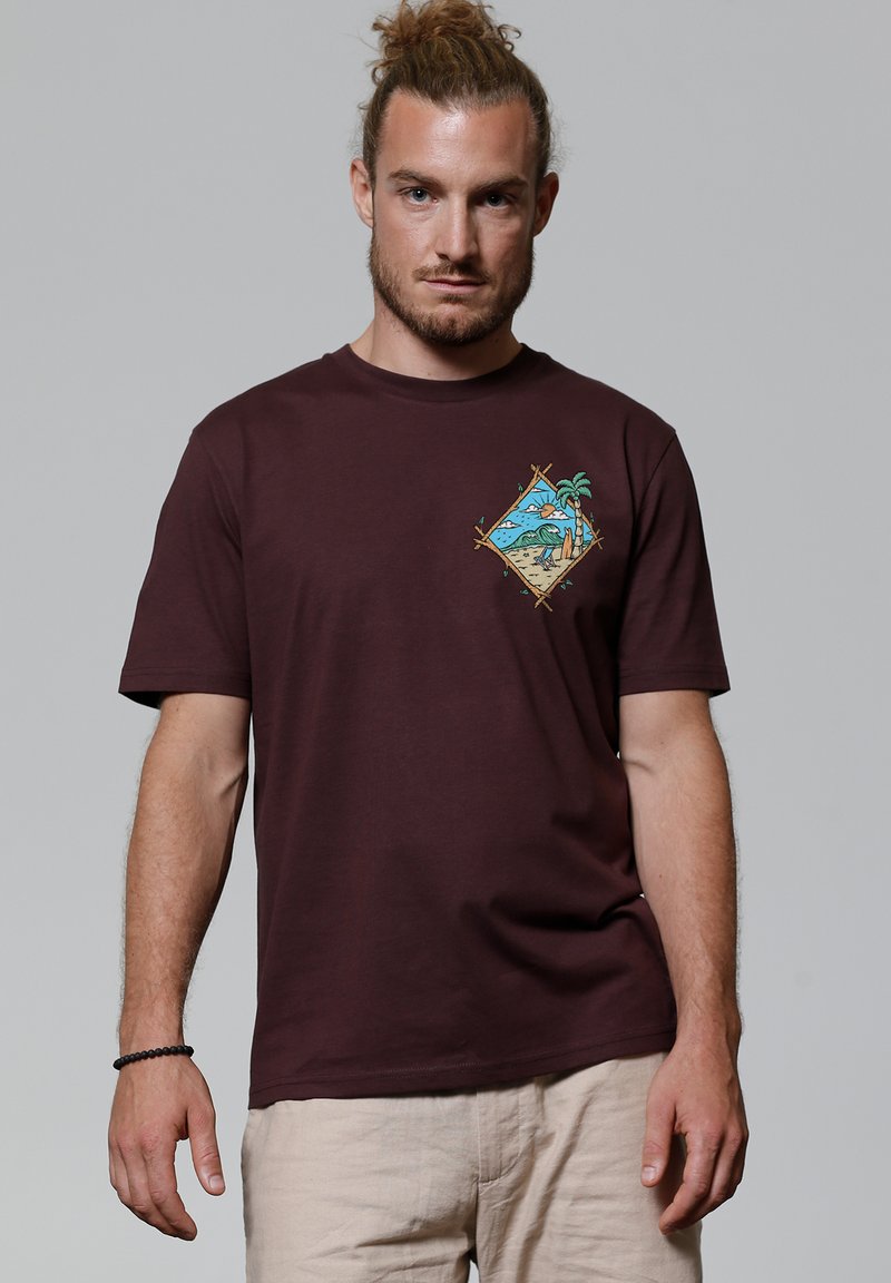 Bordeaux katoenen t-shirt met een kleurrijke gedessineerde afbeelding van palmbomen en een strand in een diamantvorm op de linkerborst.