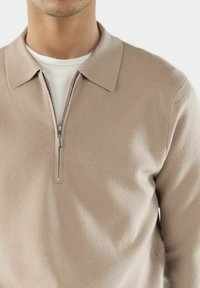 Beige, mit Reißverschluss versehener Pullover mit Kragen, aus glattem Stoff. Zeigt eine weiße Innenschicht, die am Halsausschnitt sichtbar ist. Standardpassform.