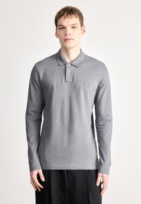 Graues Langarm-Poloshirt mit Kragen, zwei Knöpfen und einem Logo-Patch auf der linken Brust. Weicher, glatter Stoff mit einer figurbetonten Passform.