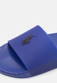 Sandalo infradito in gomma blu con una soletta testurizzata, caratterizzato da un logo nero prominente di un giocatore di polo sulla fascia. Finitura liscia, design casual.