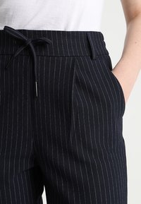 Marinblå randiga byxor med elastisk midja, dragsko och sidofickor. Mjukt tyg med en slät yta.