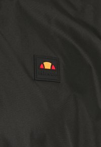 Tissu noir à la texture lisse présentant un patch logo rectangulaire en noir, rouge et jaune avec des éléments de design courbes.