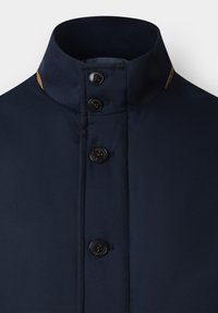 Granatowa kurtka z wysokim kołnierzem, z zapięciem na guziki, gładką fakturą i mosiężnym akcentem w pobliżu kołnierza.