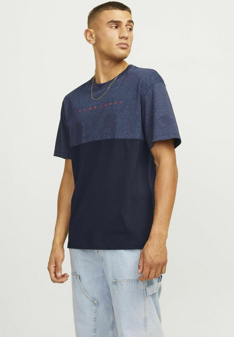 Tumesinine lühikeste varrukatega T-särk, mille ülemine osa on helesinine ja millel on punane "JACK & JONES" tekst. Pehme kangas, lõdva istuvuse ja ümmarguse kaelusega.