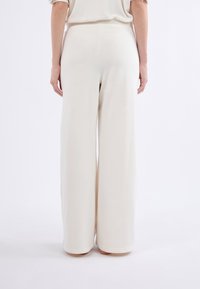 Pantalones de pierna ancha de tejido beige claro, con una textura suave y una cinturilla elástica. El diseño ofrece un ajuste holgado y una cobertura completa.