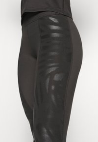 Leggings neri con un pannello testurizzato e lucido che presenta un motivo geometrico ai lati. Realizzati in materiale elasticizzato e traspirante con costruzione senza cuciture.